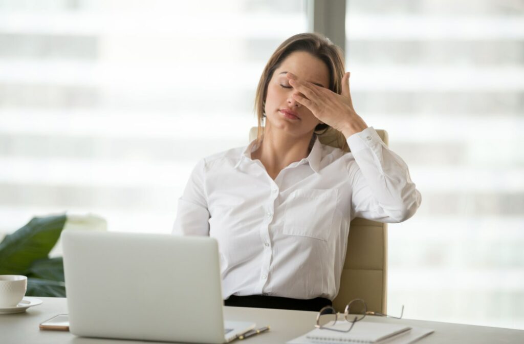 A professional-looking woman rubbing her eye while working in front of her laptop.