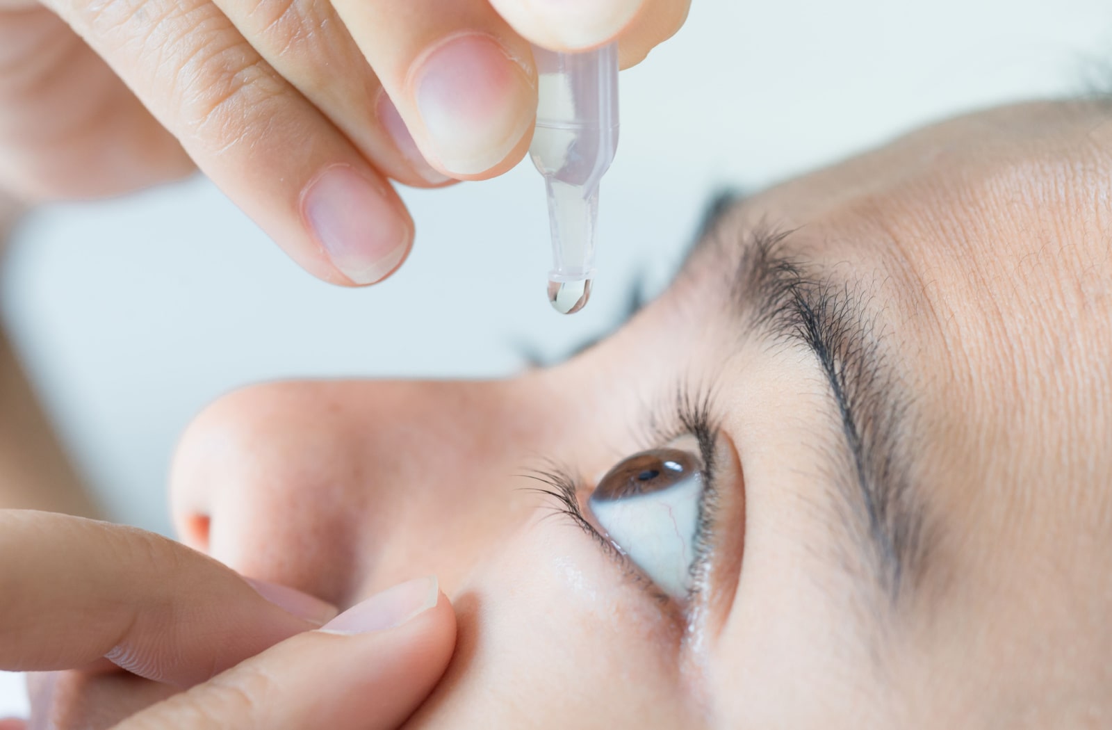 A woman putting eye drops into her eye