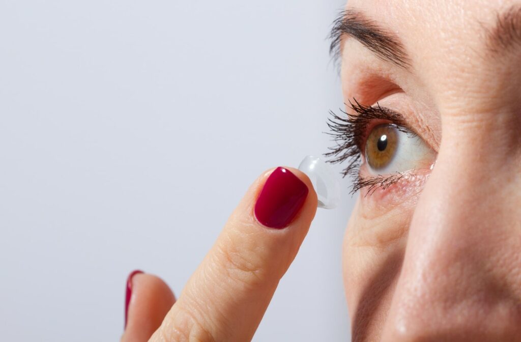 Close-up of a woman's eye with a contact lens on her index finger about to put the contact in.