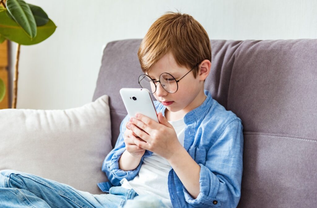 A child with myopia wearing glasses squints at a phone screen to try to see it clearly.