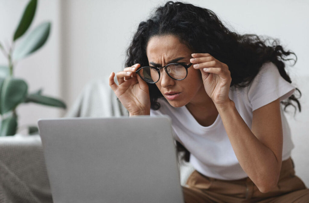 A woman adjusting her glasses and squinting to look at her computer due to her eyesight getting worse.