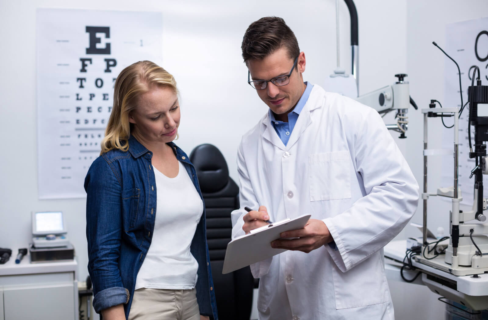 An optometrist holding a notepad, explaining to a patient after an eye exam the link between genetics and bad eyesight.