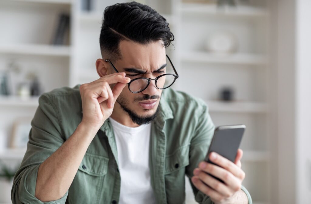 A young adult squinting and lowering their glasses to read their phone due to bad eyesight.