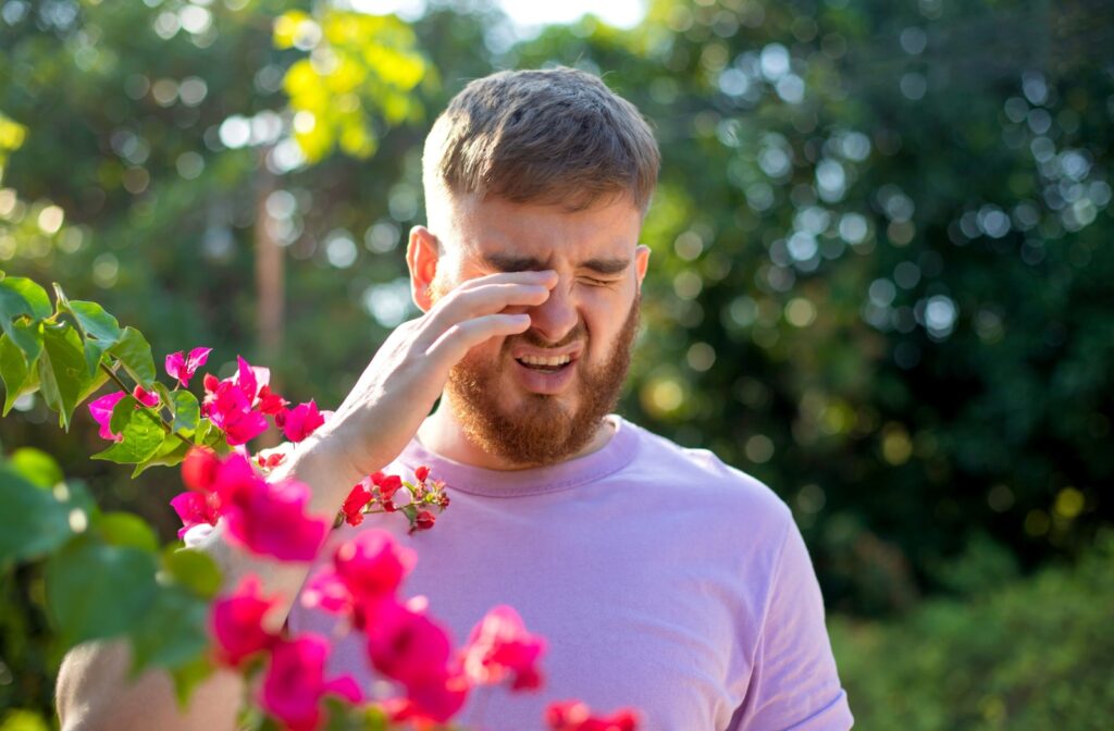 A person outdoors rubbing their eyes from eye allergies.