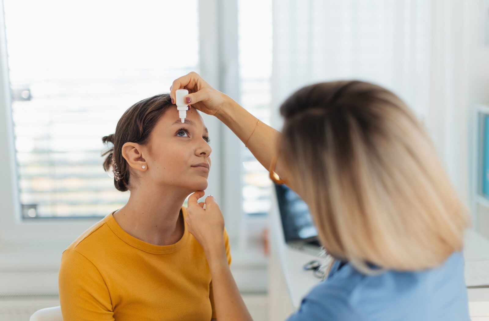 An eye doctor putting eye drops in a patient's eye to treat pink eye.