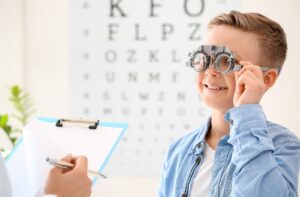 A young boy undergoing an eye exam, wearing trial lenses while smiling at the optometrist.