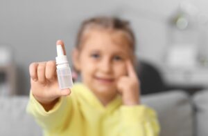 An image focused on a bottle of eye drops held by a young child in the background.