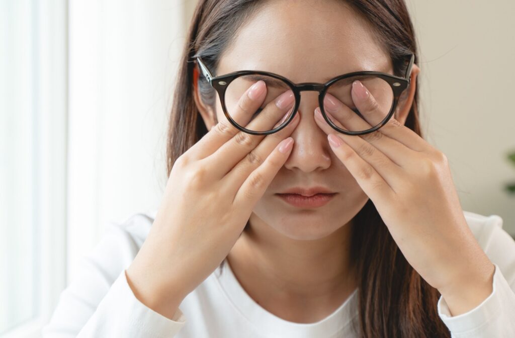 A person lifts up their glasses and covers their dry, irritated eyes.