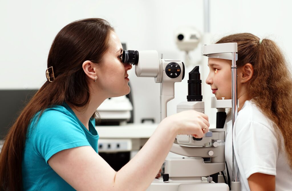 Profile of a young girl resting her head in a diagnostic tool while an optometrist examines her eye.